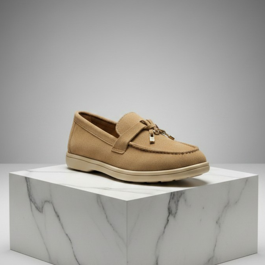 Warm tan loafer with a knotted front strap and a gold charm, on a marble block