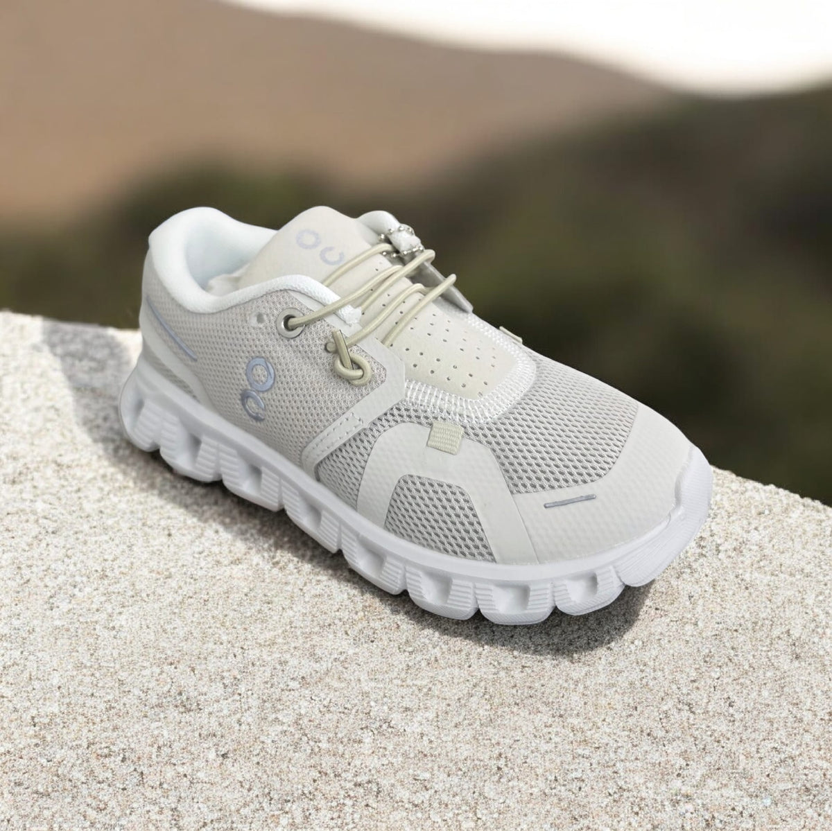 Pale grey kids runner with a toggle lace and a white wave cut sole, outdoors
