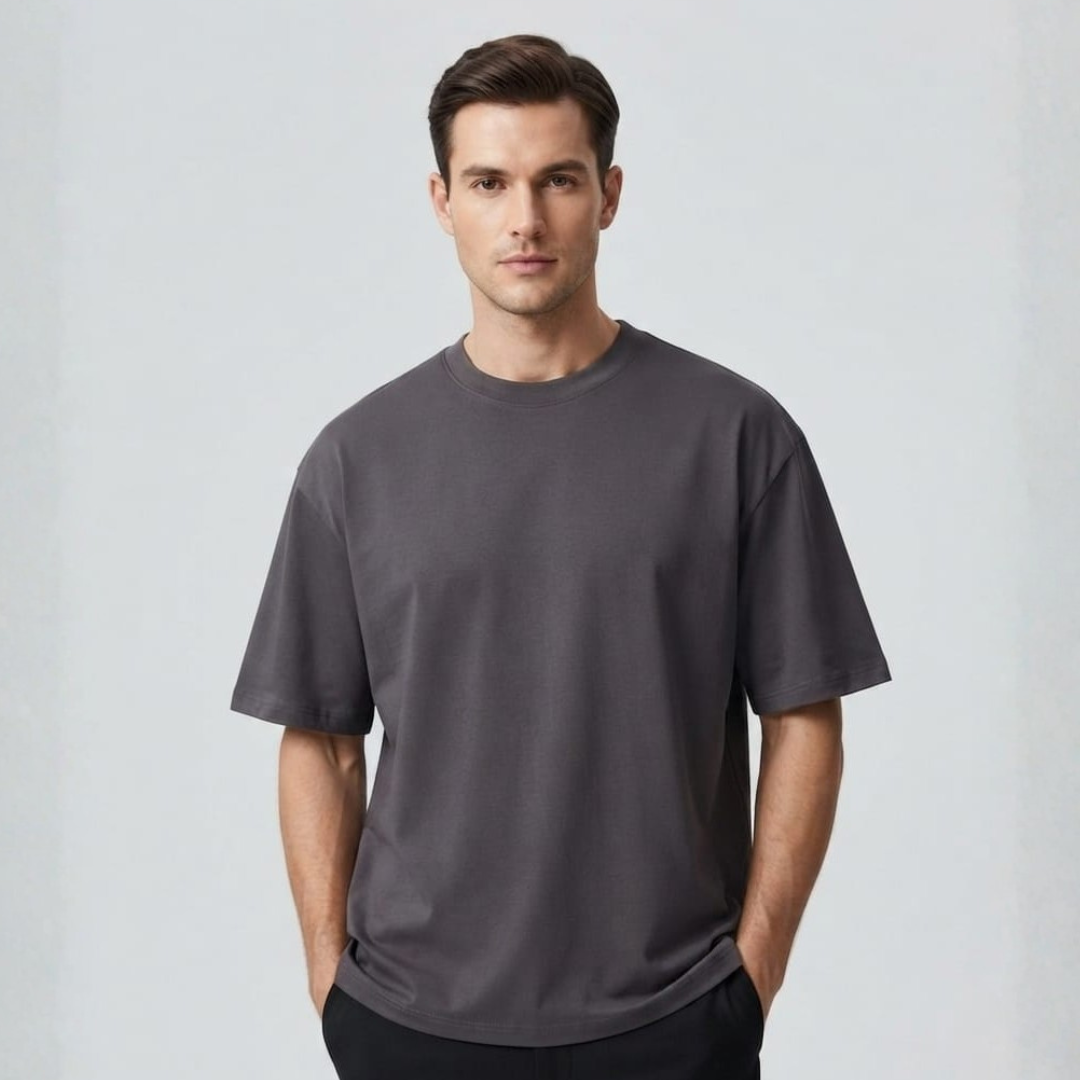 Man in a wide dark grey tee with short sleeves and a round neck, facing forward on a pale backdrop