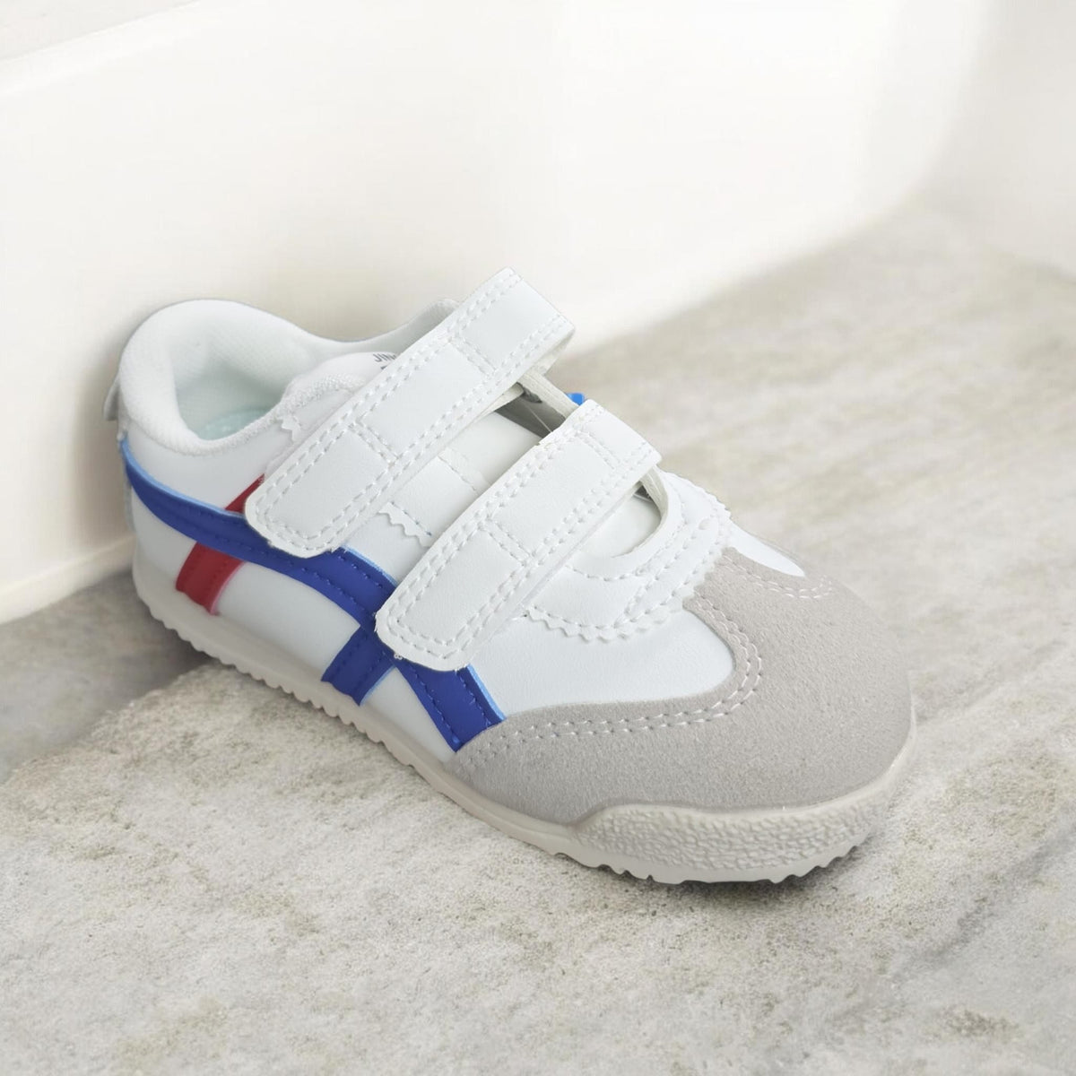 White kids trainer with two hook and loop straps, blue and red side stripes, grey toe